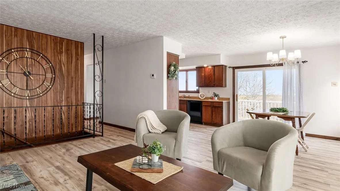 Living area featuring light wood-style floors, a textured ceiling, wooden walls, and a chandelier