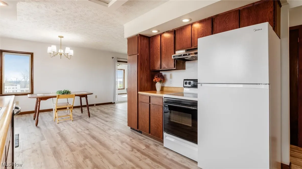 Kitchen with freestanding refrigerator, range with electric stovetop, decorative light fixtures, light countertops, and a textured ceiling
