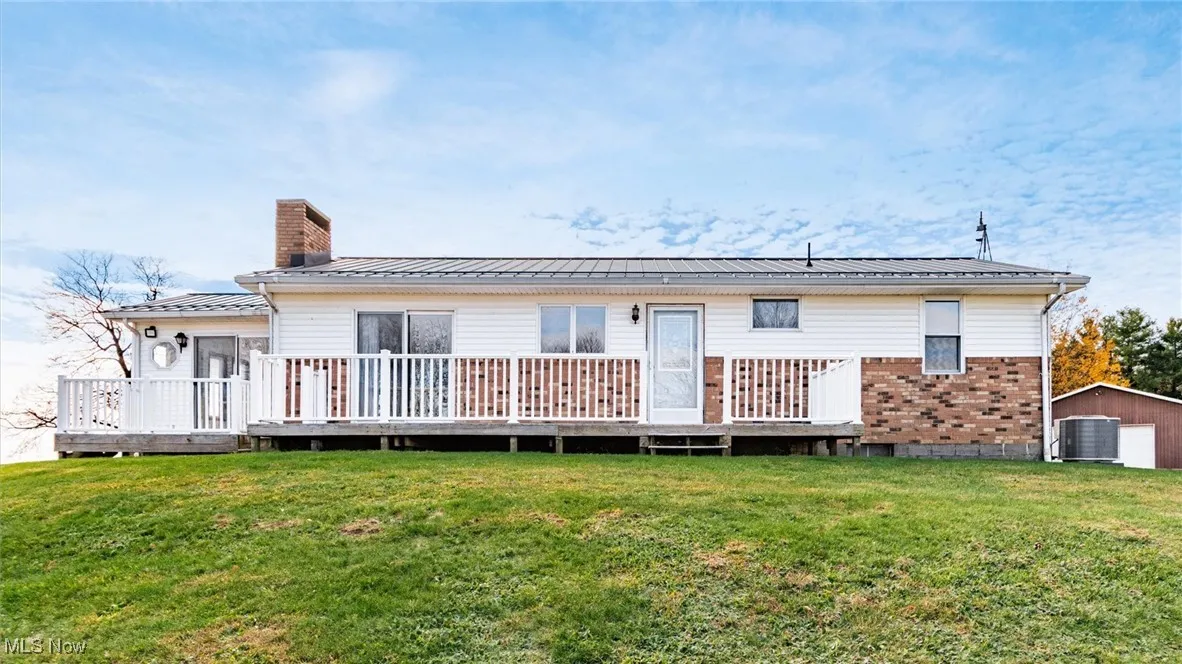 Back of property with a deck, a chimney, a metal roof, and a lawn