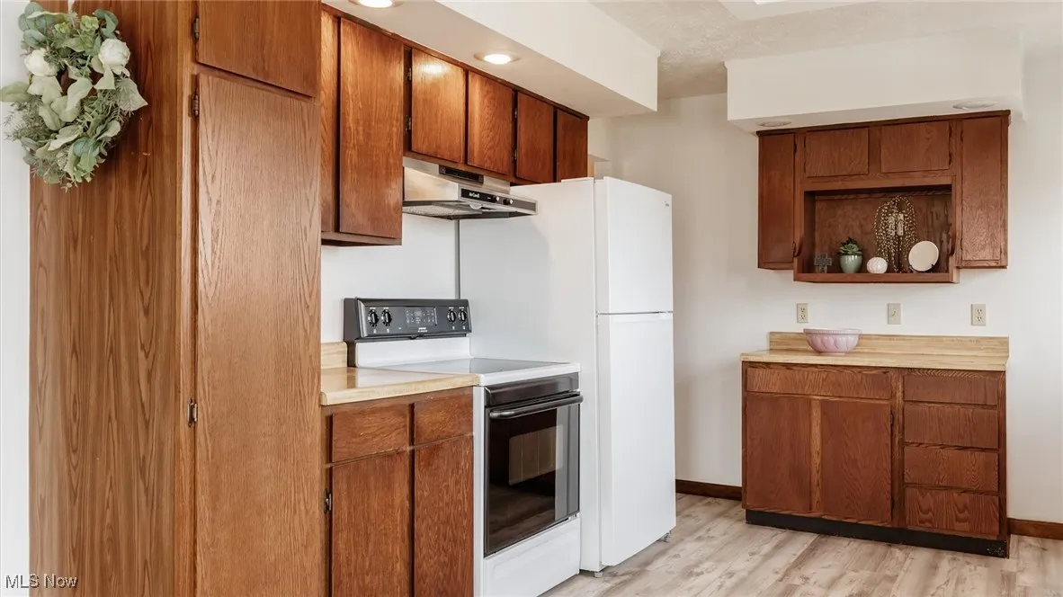 Kitchen with electric stove, light countertops, open shelves, light wood-type flooring, and under cabinet range hood