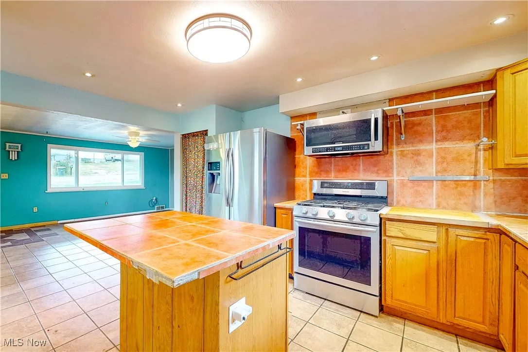Kitchen featuring appliances with stainless steel finishes, light tile patterned floors, a kitchen island, tasteful backsplash, and recessed lighting