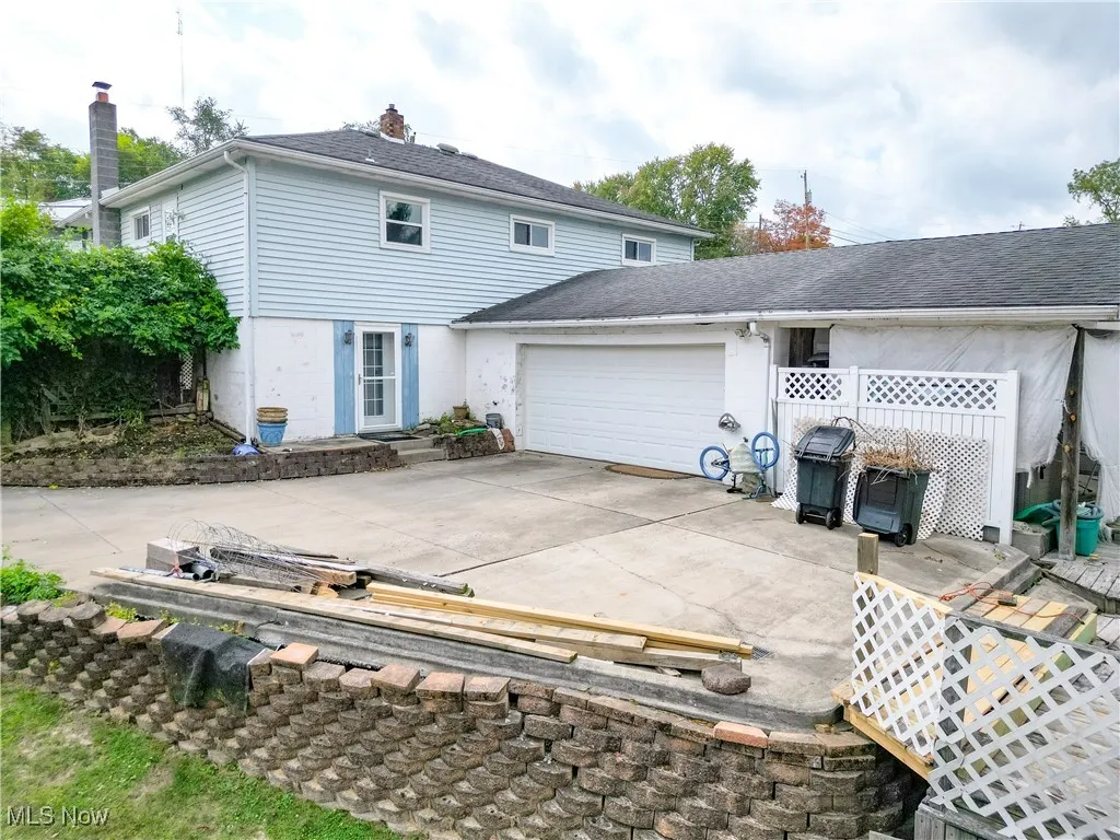 Rear view of property with a chimney, driveway, a garage, and a shingled roof