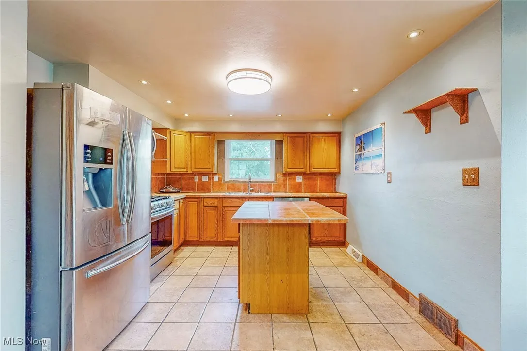 Kitchen with appliances with stainless steel finishes, light tile patterned floors, a center island, brown cabinets, and recessed lighting