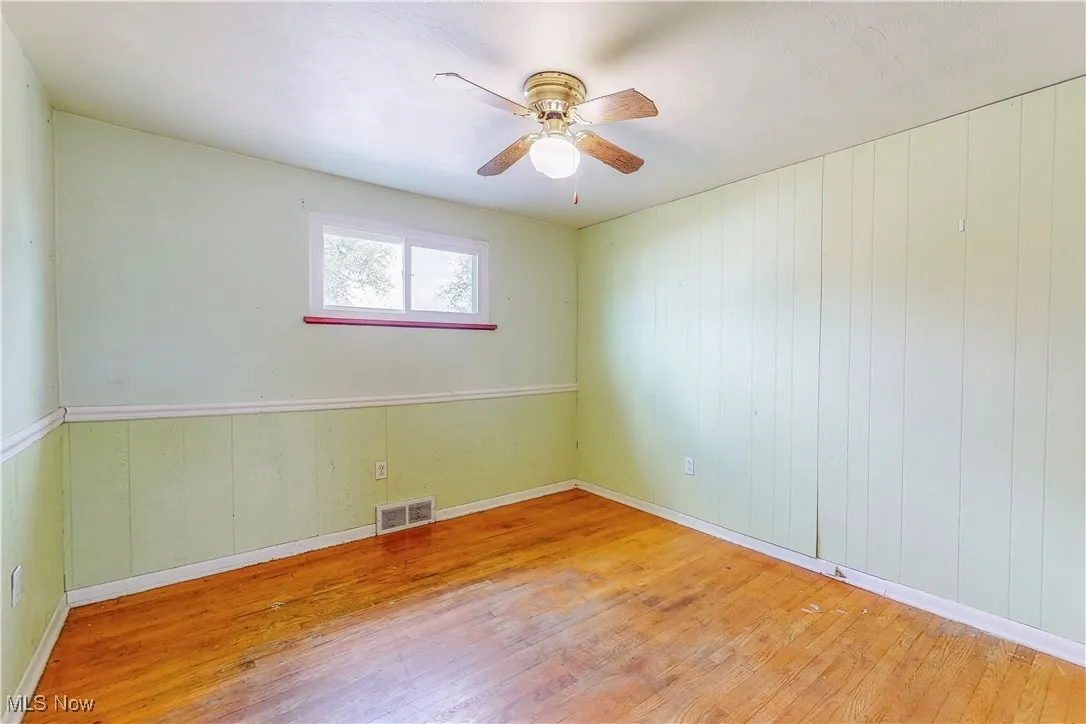 Empty room with wood finished floors, a ceiling fan, and wood walls
