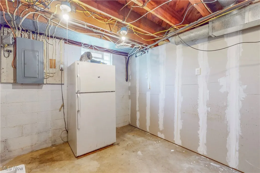 Below grade area with freestanding refrigerator and electric panel