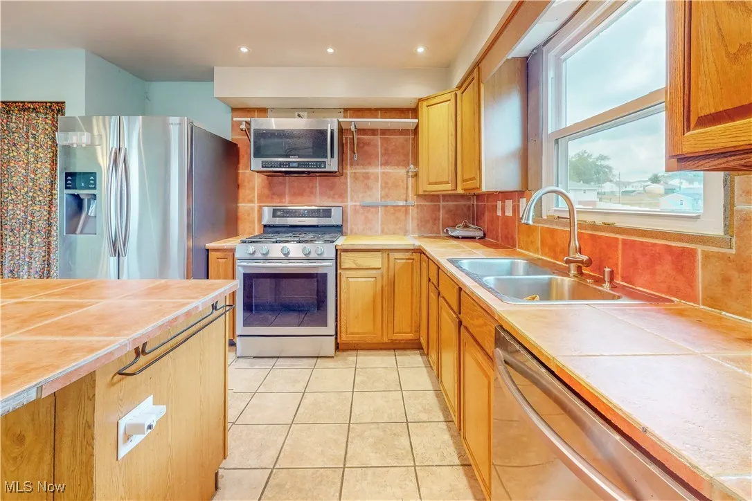 Kitchen with tile countertops, appliances with stainless steel finishes, backsplash, light tile patterned flooring, and recessed lighting