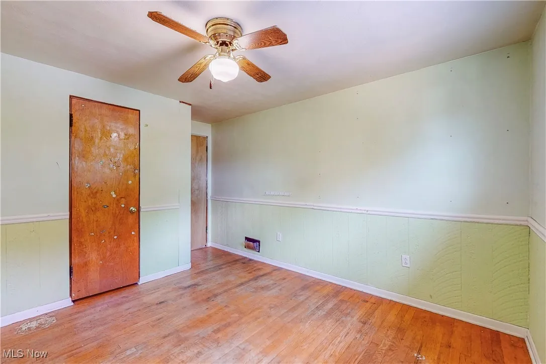 Empty room featuring hardwood / wood-style flooring, a ceiling fan, wainscoting, and wooden walls