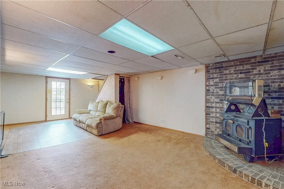 Unfurnished living room with a wood stove, carpet, and a drop ceiling