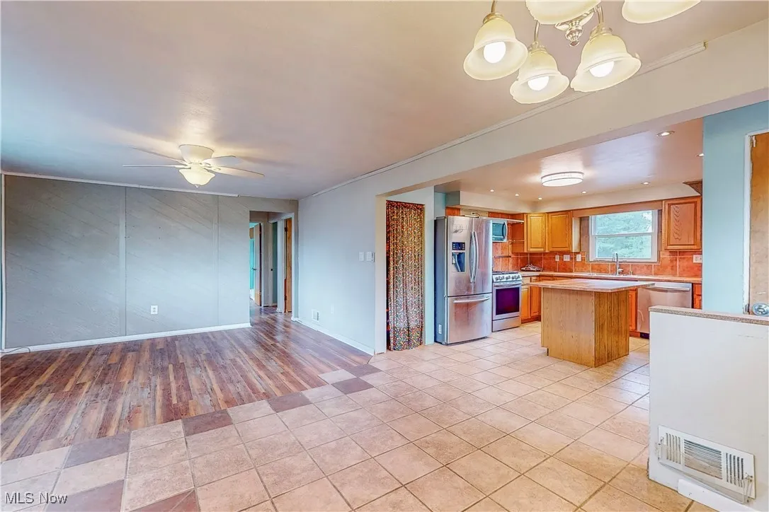 Kitchen with appliances with stainless steel finishes, light tile patterned floors, light countertops, a center island, and open floor plan