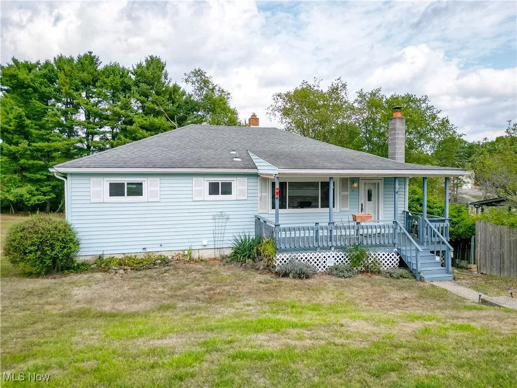 Back of property featuring a porch, a chimney, roof with shingles, and view of scattered trees