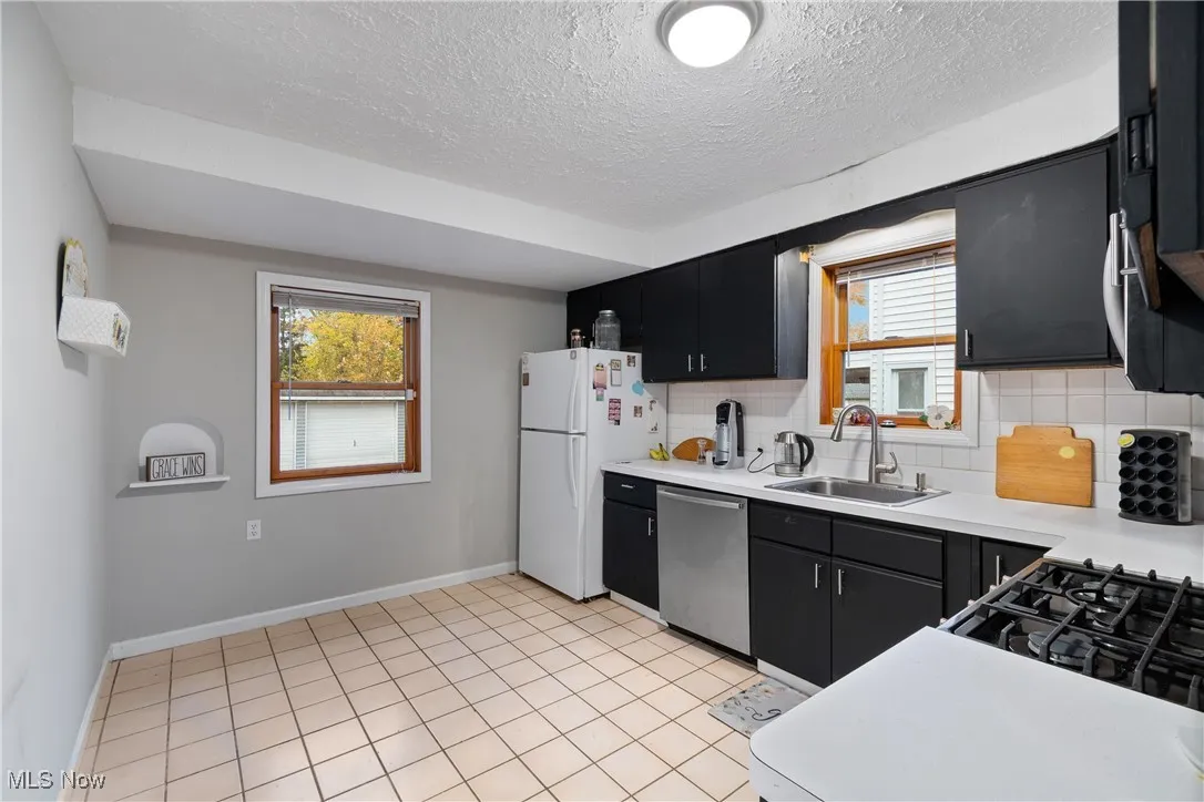Kitchen featuring dark cabinetry, light countertops, freestanding refrigerator, tasteful backsplash, and dishwasher