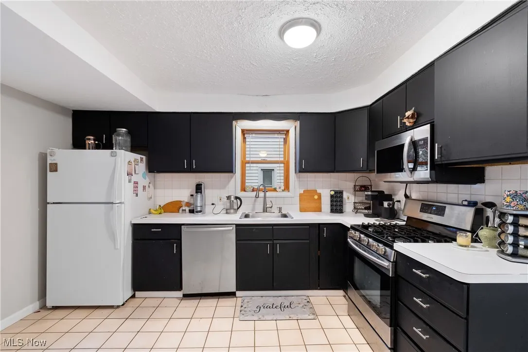 Kitchen with dark cabinetry, appliances with stainless steel finishes, backsplash, and a textured ceiling