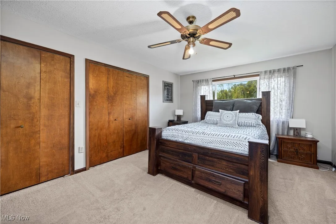 Bedroom featuring two closets, light colored carpet, ceiling fan, and a textured ceiling