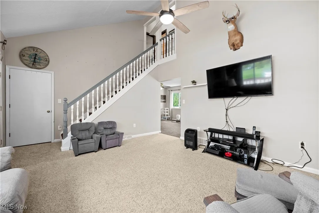 Carpeted living room featuring high vaulted ceiling, ceiling fan, and stairway