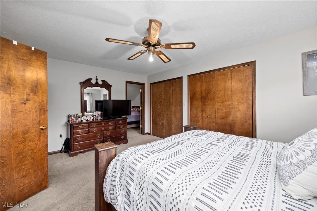 Carpeted bedroom featuring multiple closets, a ceiling fan, and a textured ceiling