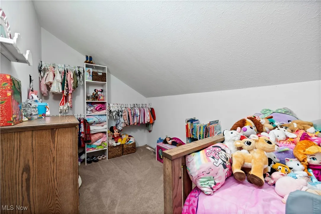 Bedroom with a textured ceiling, carpet flooring, and lofted ceiling