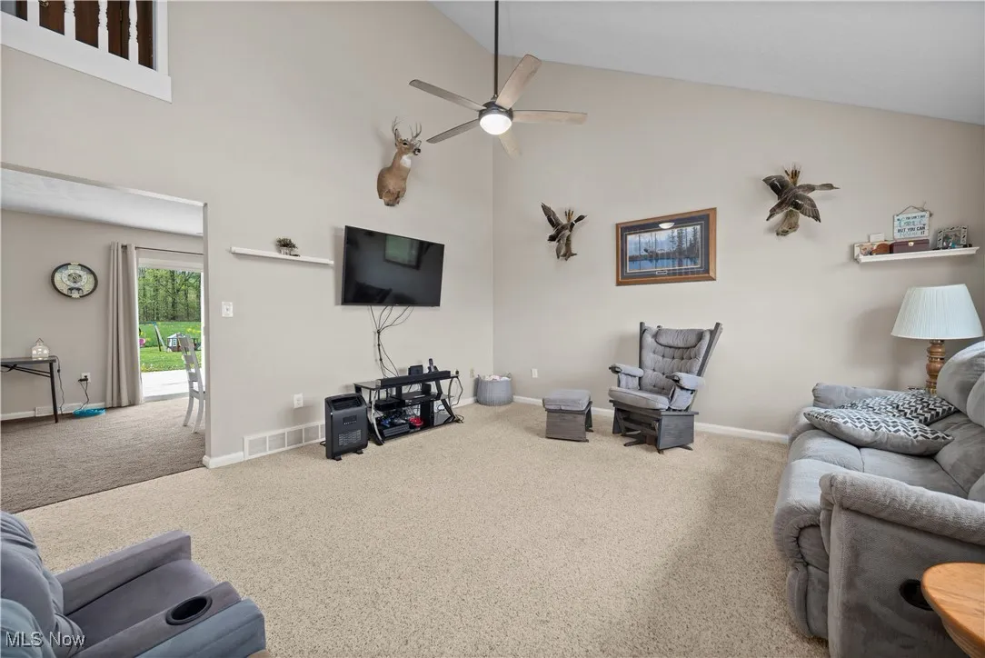 Carpeted living room featuring high vaulted ceiling and a ceiling fan