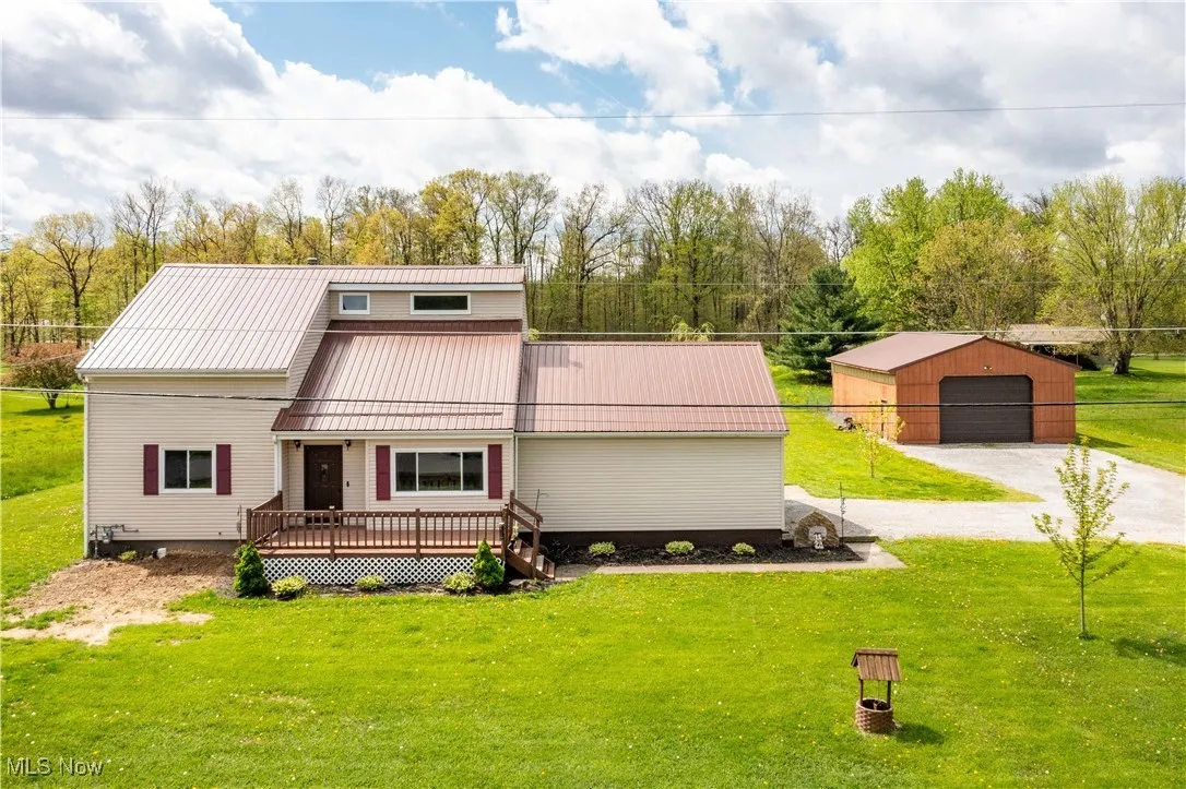 View of front of property with a front yard, a wooden deck, an outbuilding, a metal roof, and a garage