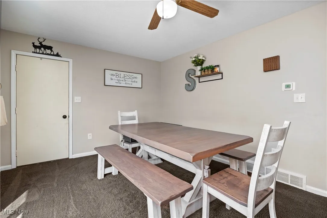 Dining space with dark colored carpet and a ceiling fan