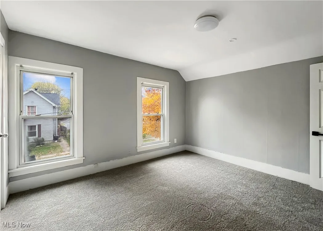 Carpeted spare room with vaulted ceiling and baseboards