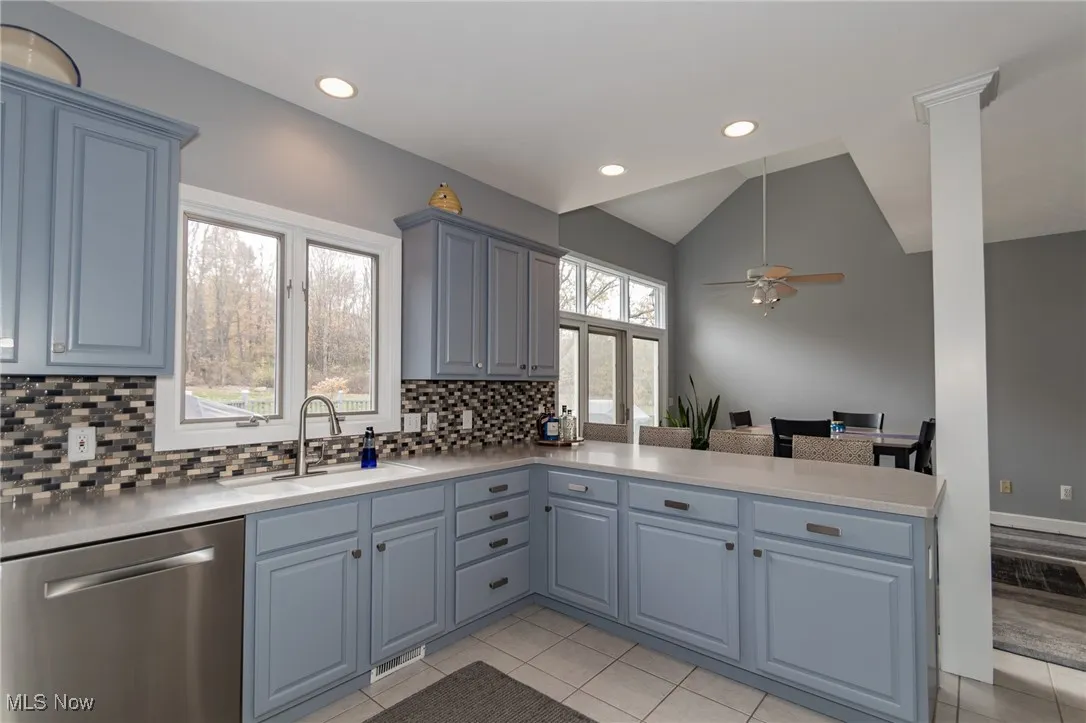 Kitchen with a peninsula, dishwasher, light tile patterned floors, lofted ceiling, and ceiling fan