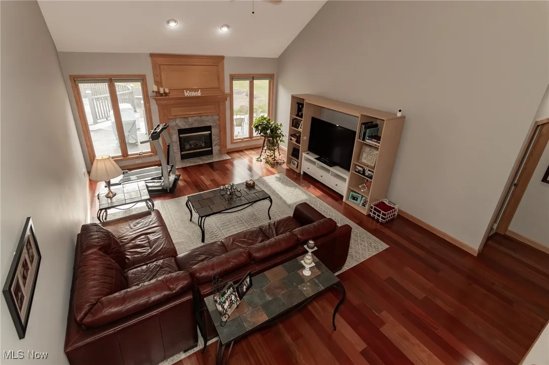 Living area featuring dark wood-style flooring, a premium fireplace, ceiling fan, and high vaulted ceiling
