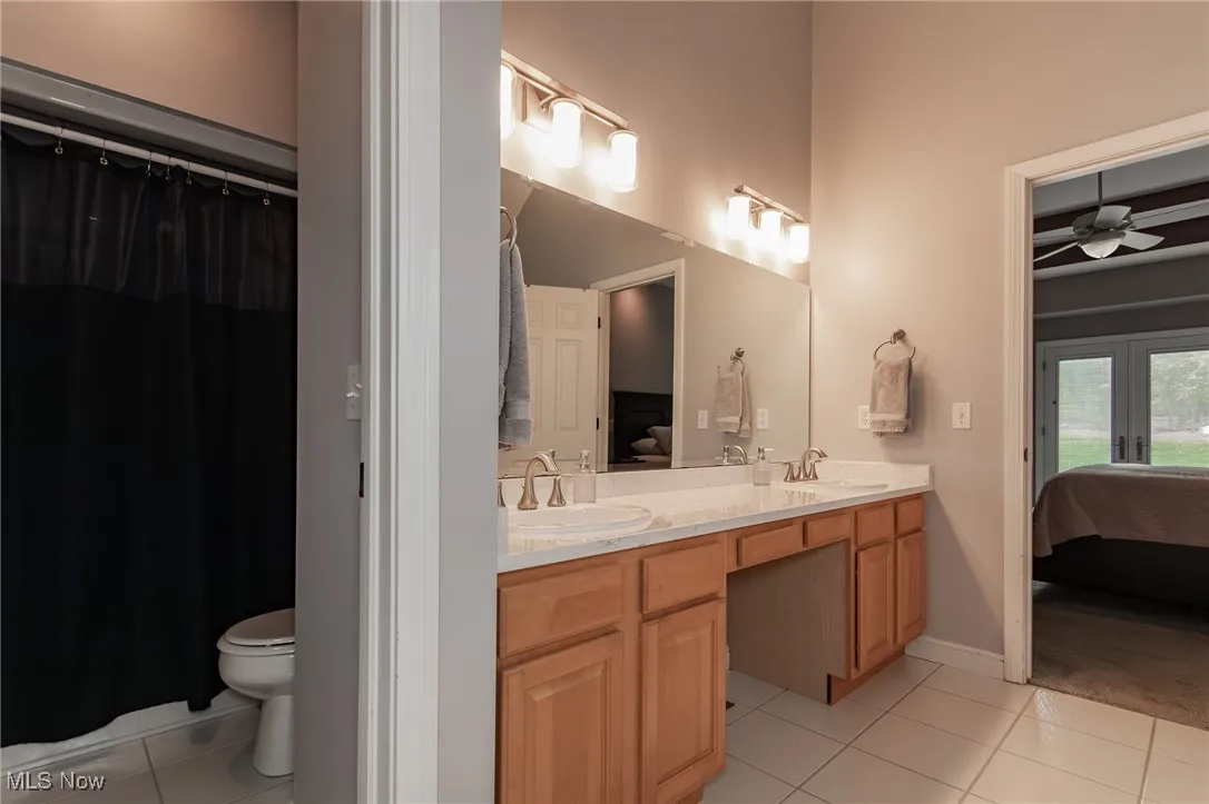 Ensuite bathroom with light tile patterned floors, double vanity, ceiling fan, and a shower with shower curtain