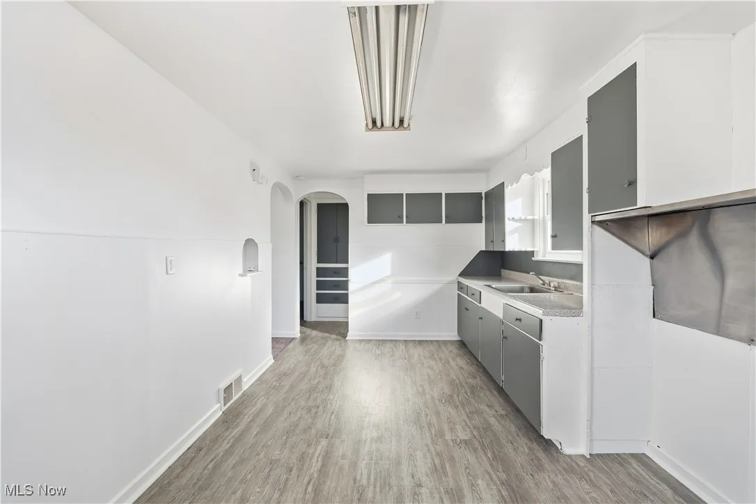 Kitchen with gray cabinets, light wood-style flooring, arched walkways, and light countertops