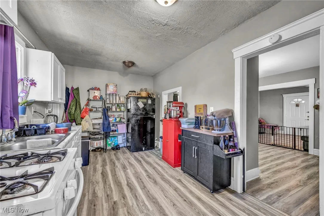 Kitchen with white gas range, light wood finished floors, a textured ceiling, light countertops, and white cabinetry