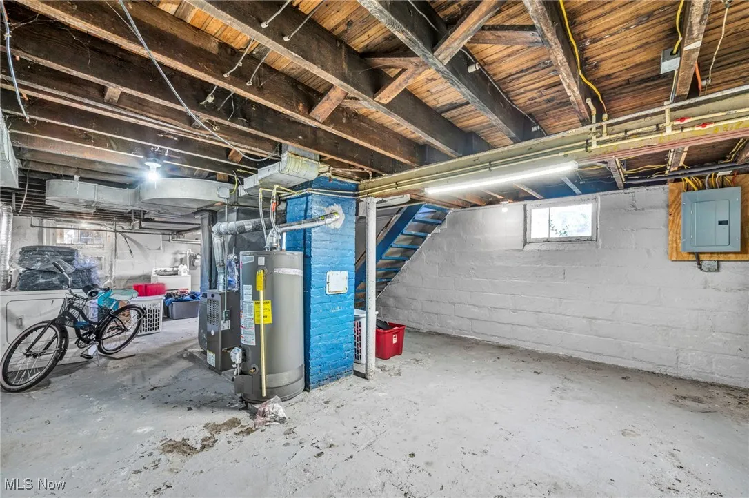 Below grade area featuring electric panel, water heater, and stairway