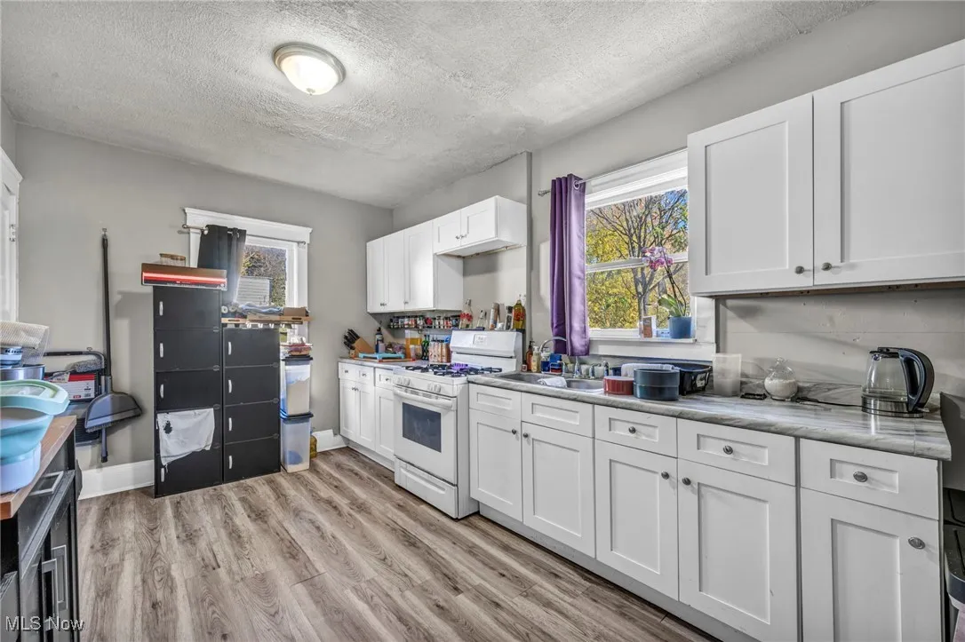 Kitchen featuring a textured ceiling, white gas range, white cabinetry, light wood-type flooring, and light countertops