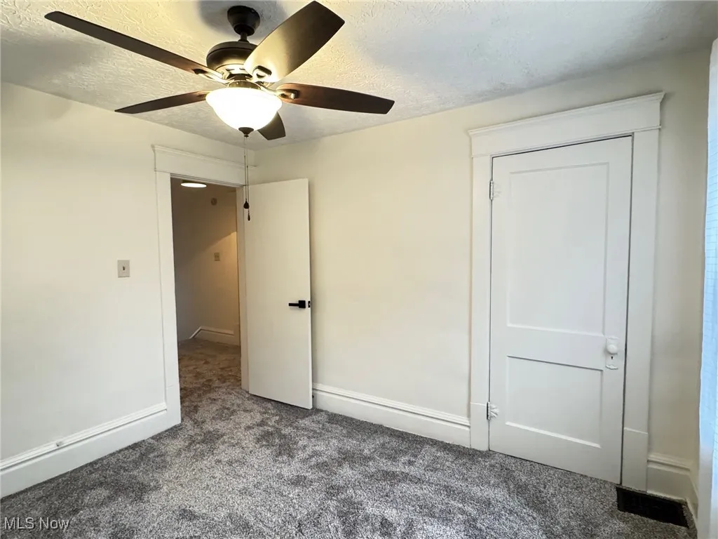 Unfurnished bedroom featuring a textured ceiling, carpet floors, and a ceiling fan