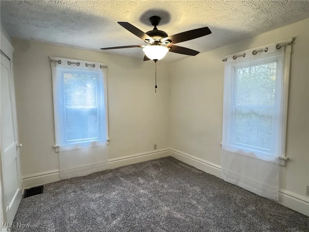 Empty room featuring dark carpet, a textured ceiling, and ceiling fan
