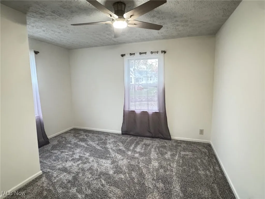 front bedroom with dark colored carpet, a textured ceiling, and a ceiling fan