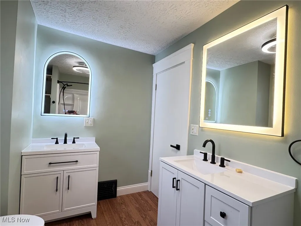 Full bath featuring a textured ceiling, two vanities, dark wood-style floors, and a shower with curtain