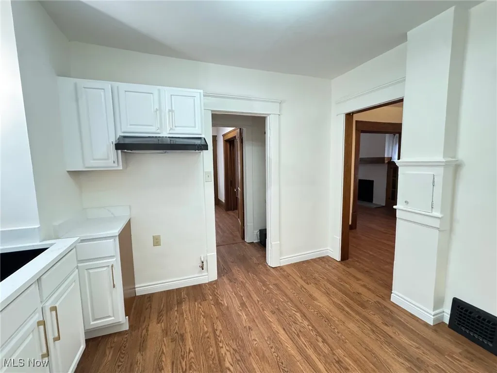 Kitchen with dark wood-type flooring, white cabinets, light stone countertops, and under cabinet range hood