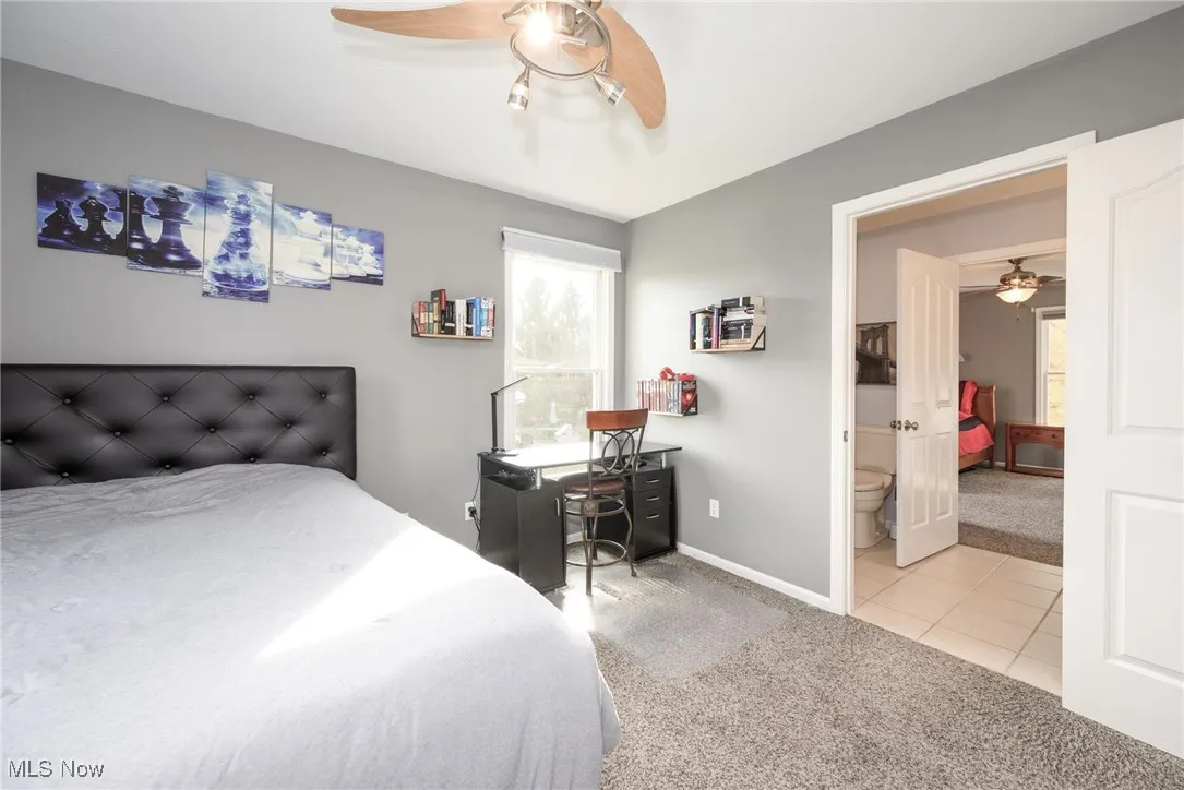 Bedroom featuring light colored carpet, light tile patterned floors, a ceiling fan, and ensuite bathroom