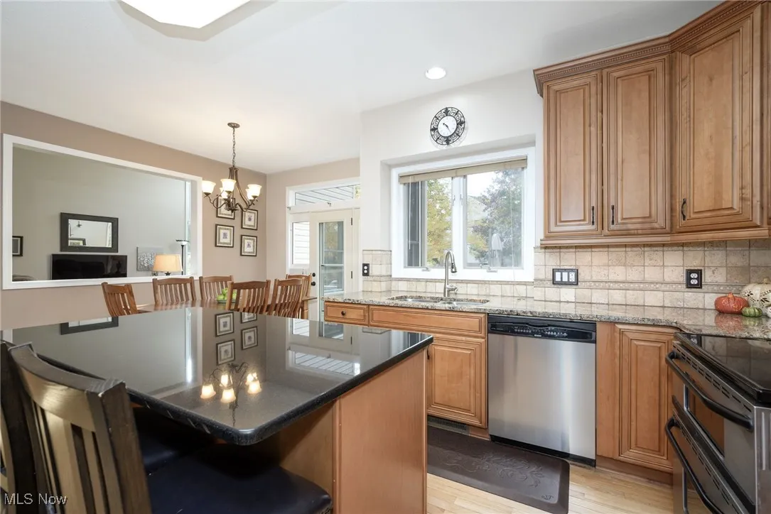Kitchen with brown cabinetry, dark stone counters, stainless steel appliances, a kitchen breakfast bar, and recessed lighting