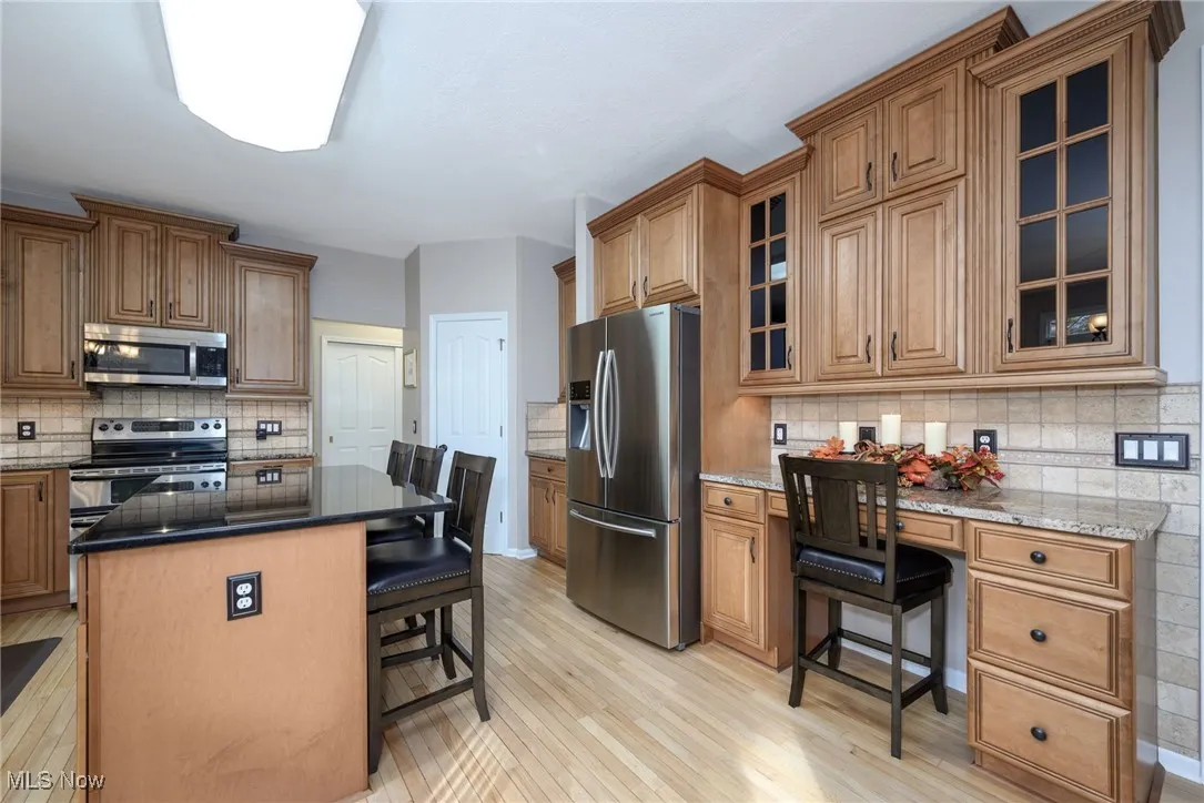 Kitchen with a kitchen breakfast bar, brown cabinetry, stainless steel appliances, dark stone countertops, and backsplash