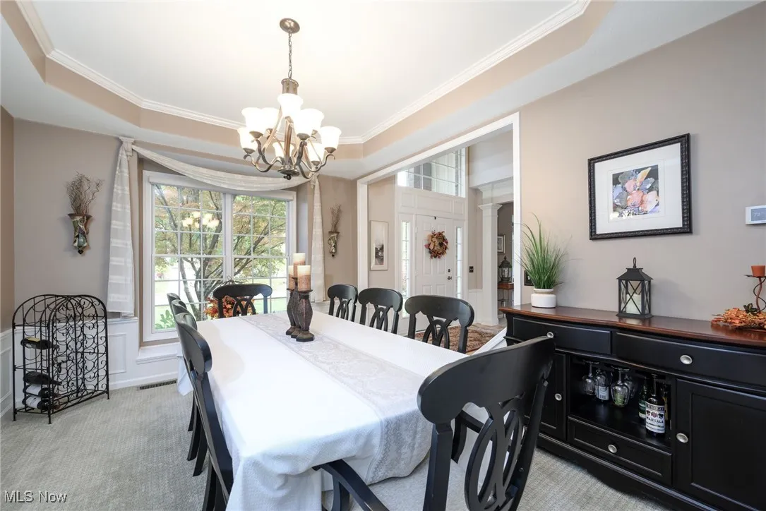 Dining area with a tray ceiling, crown molding, light colored carpet, and a chandelier