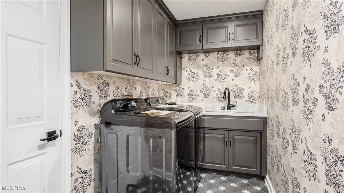 Laundry area with independent washer and dryer, wallpapered walls, and cabinet space