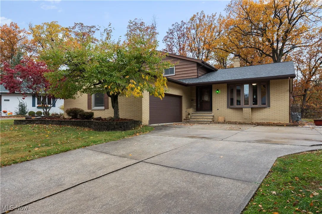 View of front facade with driveway, brick siding, a garage, a chimney, and a front lawn