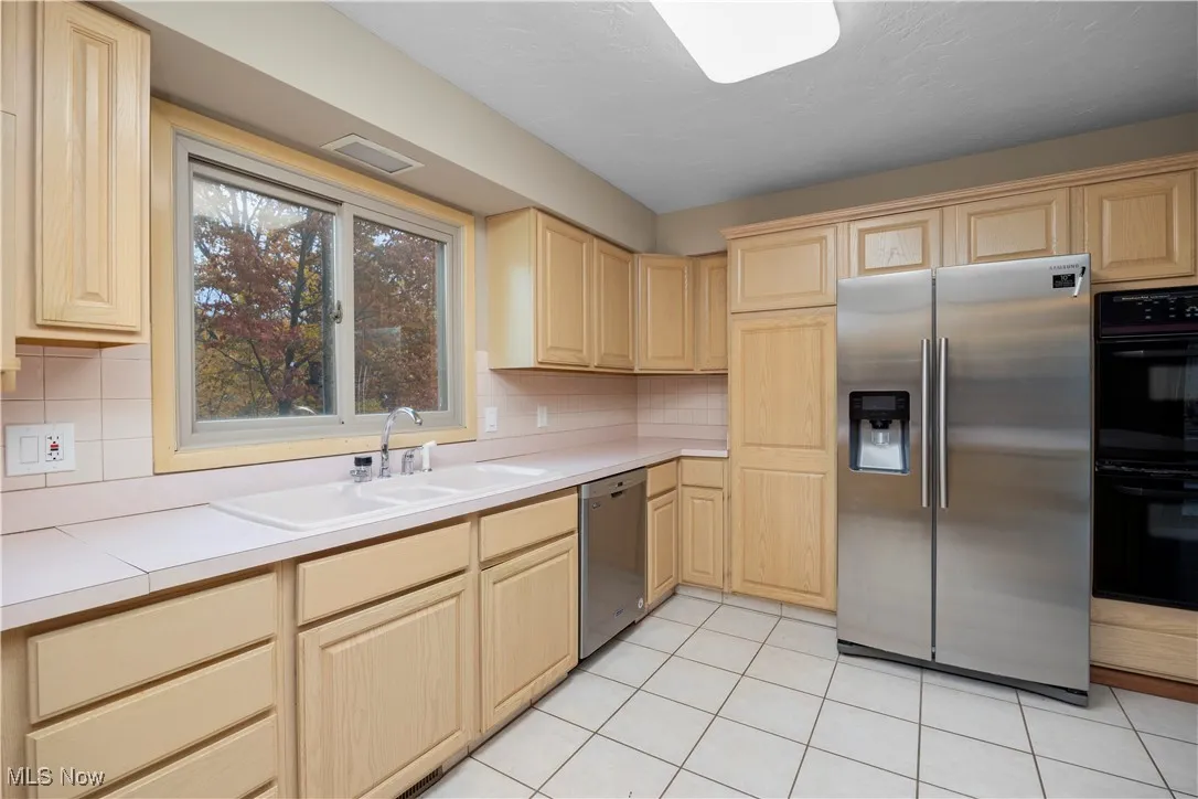 Kitchen with stainless steel appliances, light brown cabinets, and light tile patterned floors