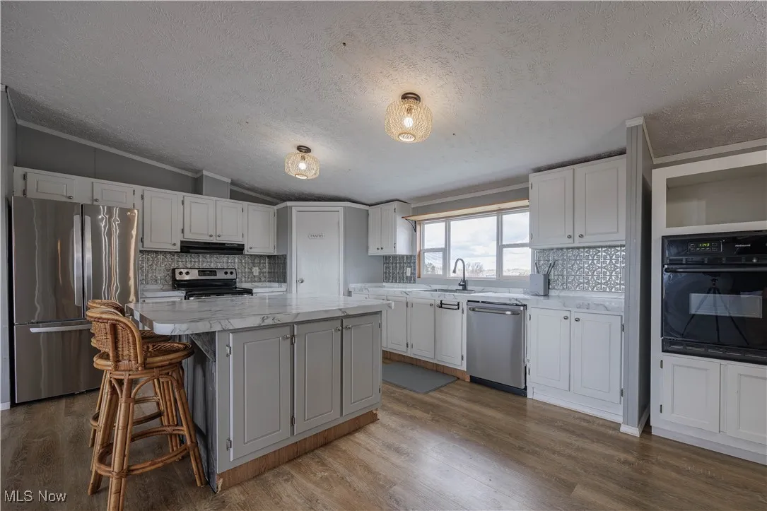 Kitchen featuring stainless steel appliances, a textured ceiling, dark wood-style floors, tasteful backsplash, and vaulted ceiling