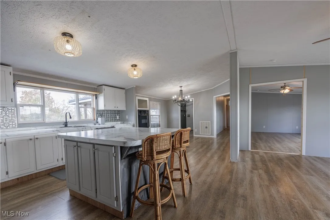 Kitchen featuring crown molding, dark wood-style flooring, a kitchen island, a kitchen breakfast bar, and a ceiling fan
