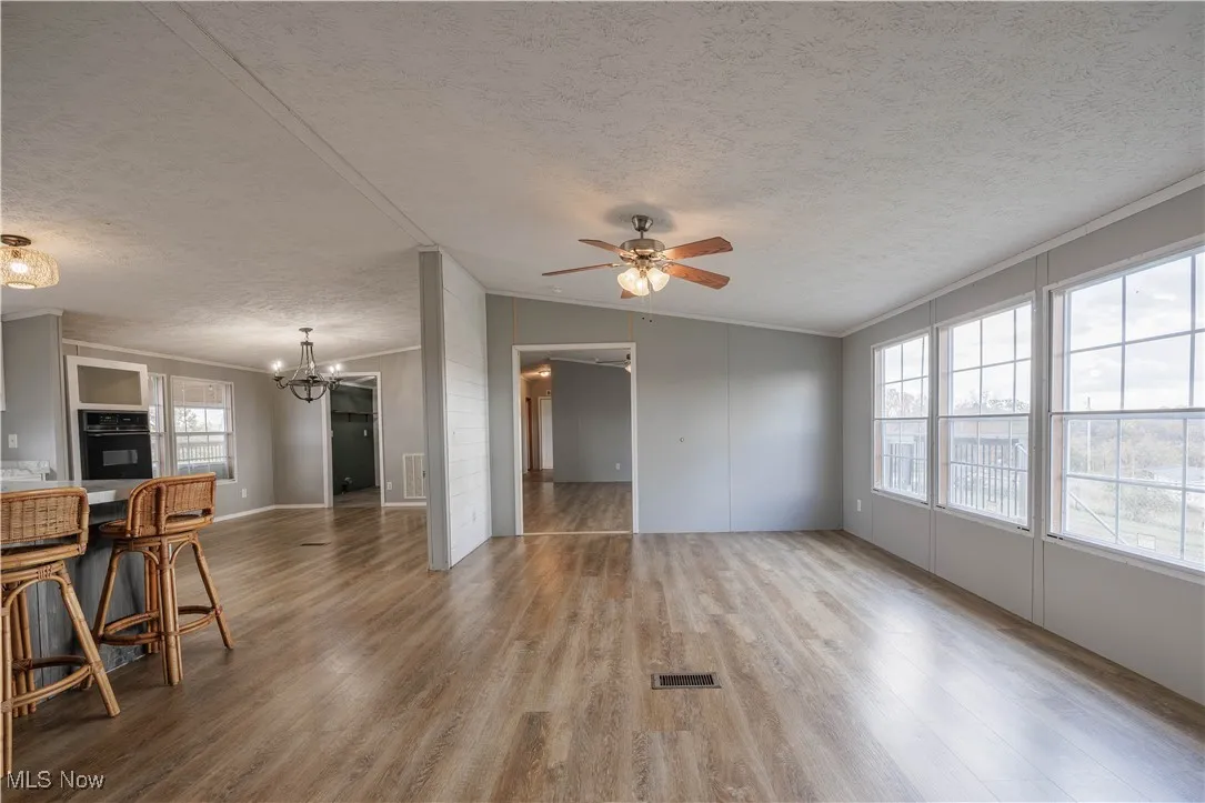 Living area featuring a textured ceiling, ornamental molding, wood finished floors, a chandelier, and a ceiling fan