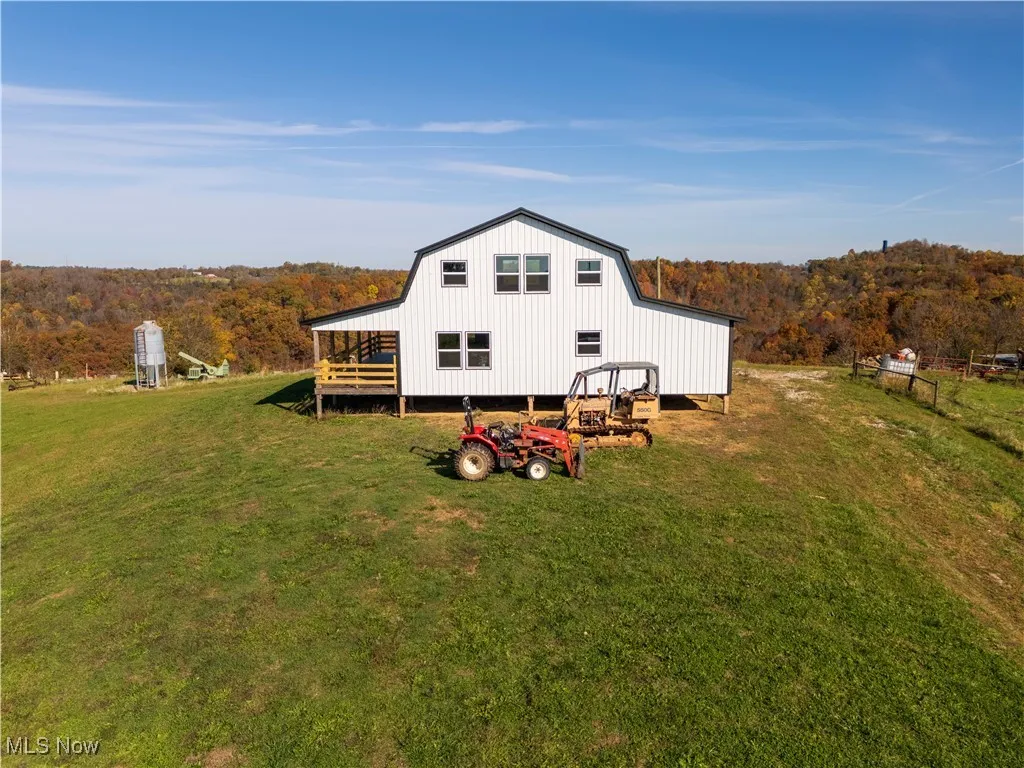 Rear view of house with a yard, a view of trees, a wooden deck, and a gambrel roof