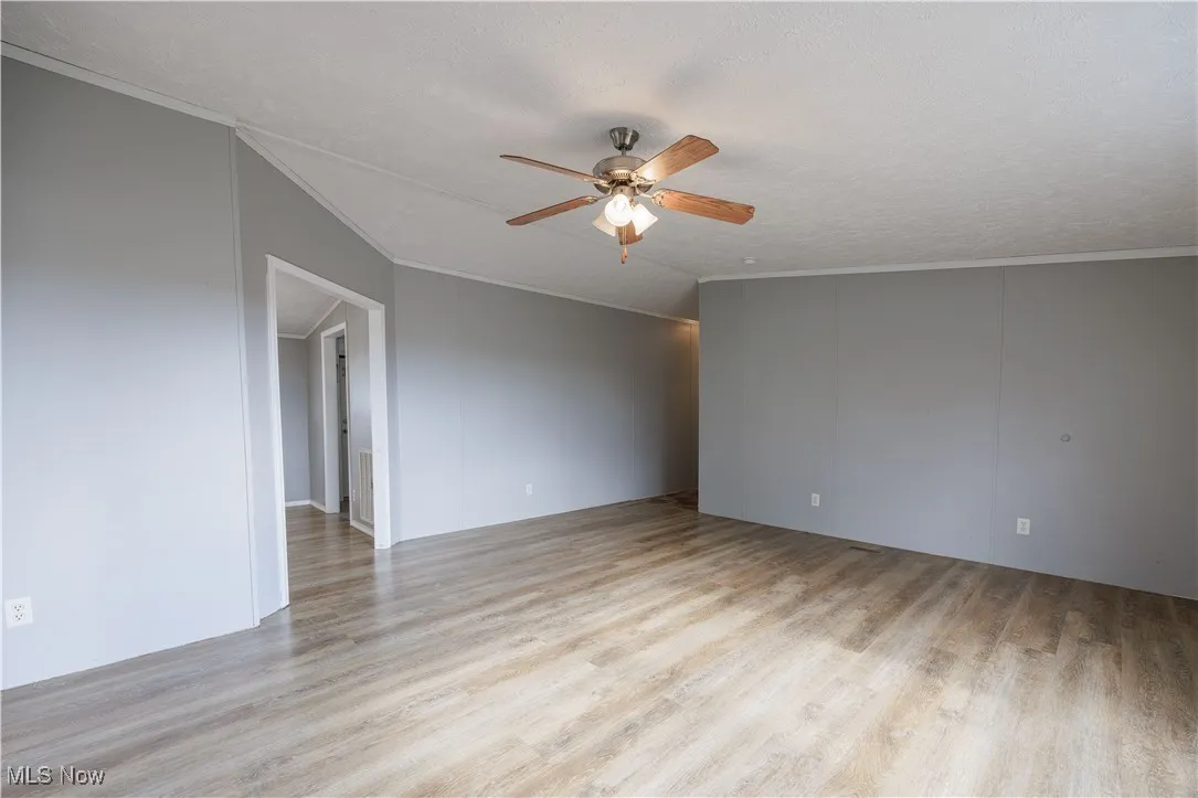 Spare room with crown molding, light wood-style flooring, a textured ceiling, and a ceiling fan