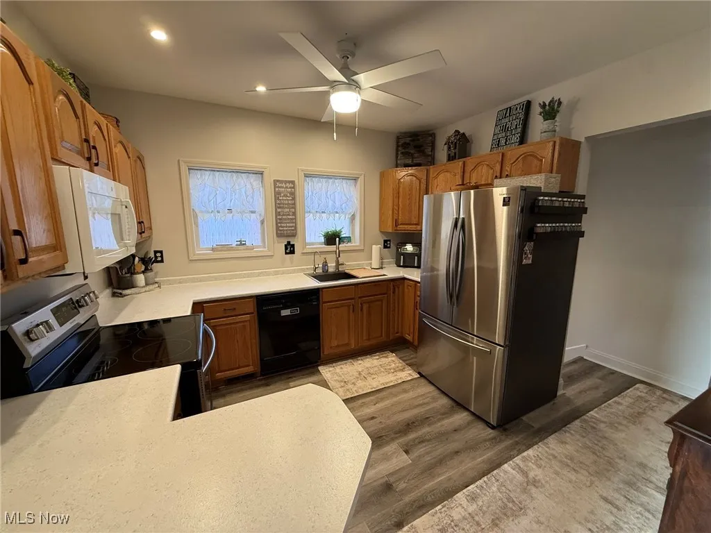 Kitchen with appliances with stainless steel finishes, dark wood-style flooring, a ceiling fan, recessed lighting, and brown cabinetry