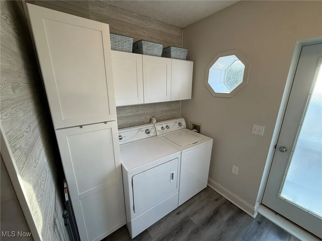 Laundry area with cabinet space, dark wood-type flooring, washer and clothes dryer, and a textured ceiling
